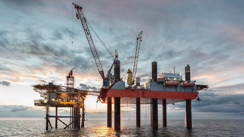 A cloe-up of an oil rig in the ocean at sunset.